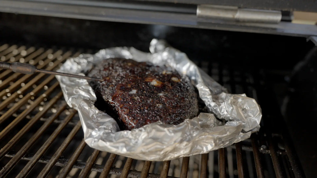 Brisket wrapped in foil on the smoker, probed for temperature